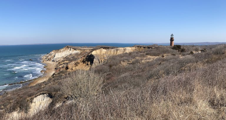 Beautiful coastal scenery with the Aquinnah lighthouse and cliffs under a clear blue sky.