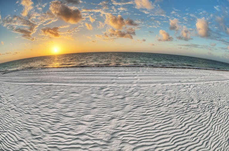Experience the tranquil beauty of a beach sunrise with golden sun, soft sand, and scattered clouds over the ocean.