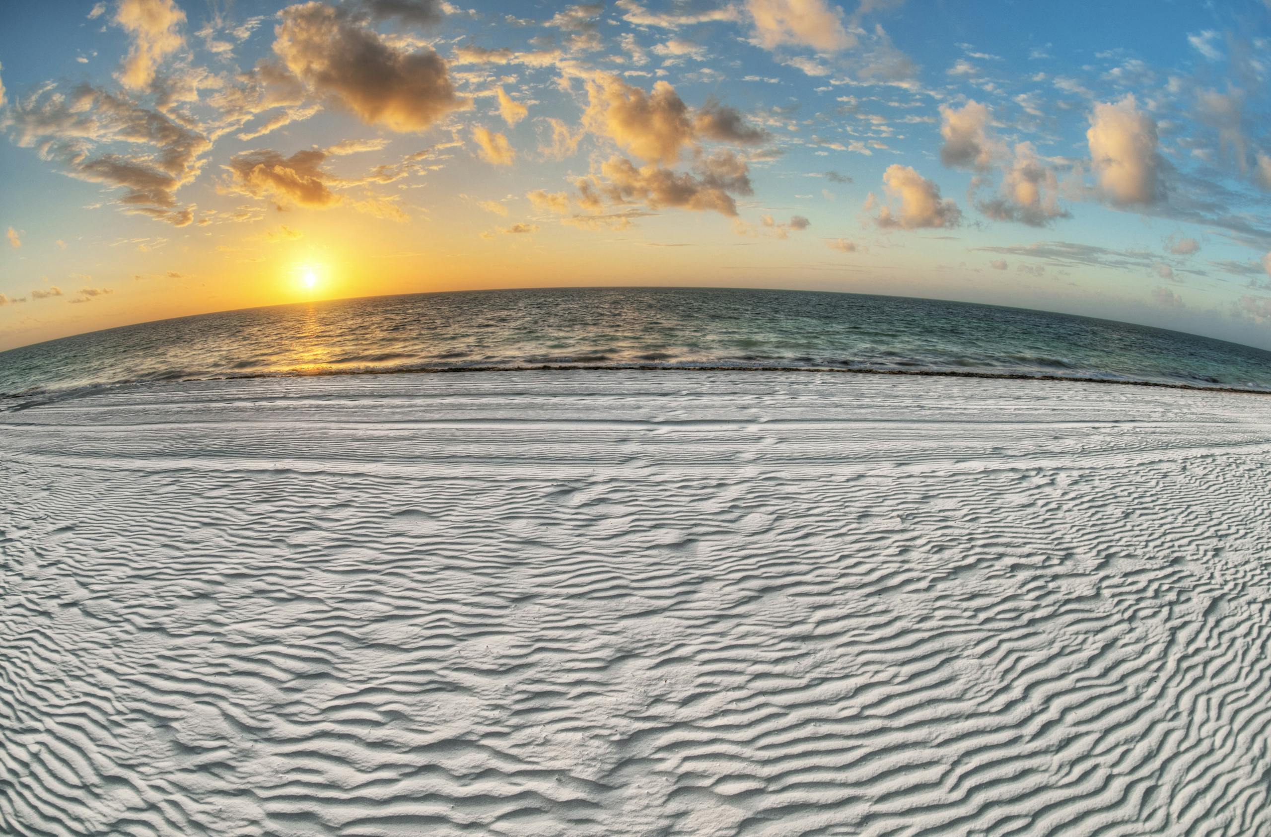 Experience the tranquil beauty of a beach sunrise with golden sun, soft sand, and scattered clouds over the ocean.